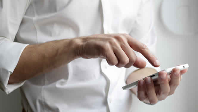 Man wearing a white business shirt holding a mobile phone. He is dialing a number.