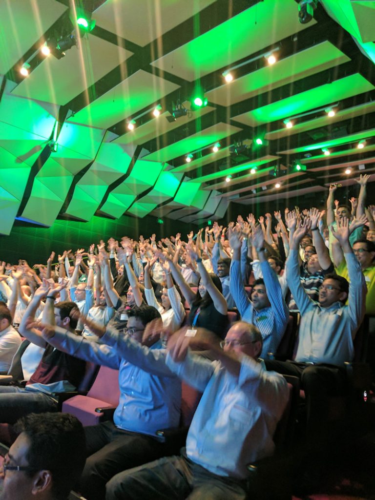 Photo of a conference room full of people seated with their arms up in the air.